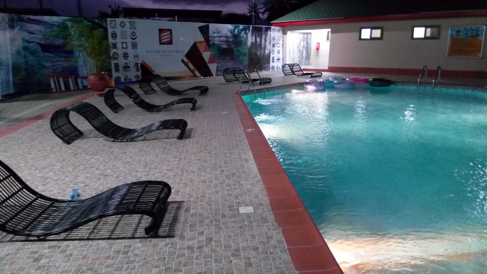 Outdoor pool at night with loungers and an Adinkra-symbol feature wall